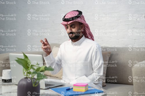 رجل سعودي يرتدي الزي السعودي الرسمي يجلس أمام جهاز الأبتوب يتحدث مع أحدهم بلغة الإشارة