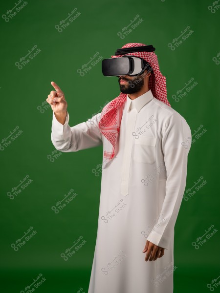 رجل يرتدي الثوب السعودي يقف مستخدمًا نظارة الواقع الافتراضي أمام خلفية خضراء.