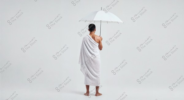 The image shows a person standing with a white towel wrapped around their body, holding a white umbrella. The background is white, creating a simple and calm atmosphere.