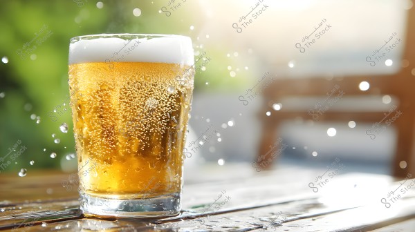 A glass cup filled with a sparkling fizzy drink topped with white foam, placed on a wooden table. The golden beverage beautifully reflects the light, with water droplets scattered around the glass, adding a refreshing feel. The background is blurred with gradients of green and beige, suggesting an outdoor natural environment under sunlight.