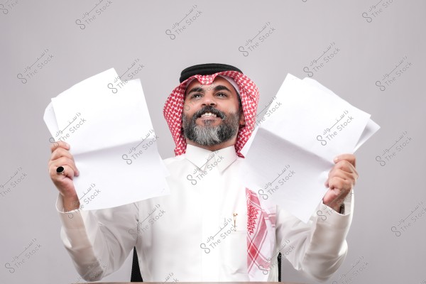 رجل يرتدي الزي التقليدي الخليجي ويمسك بأوراق بيضاء بيده, يبدو سعيدًا.