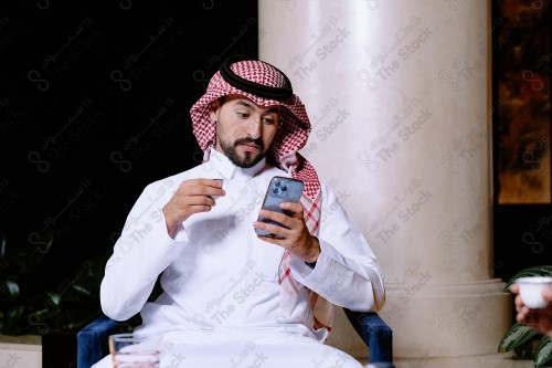 شاب سعودي يرتدي الزي السعودي التقليدي يستخدم جواله في المقهى