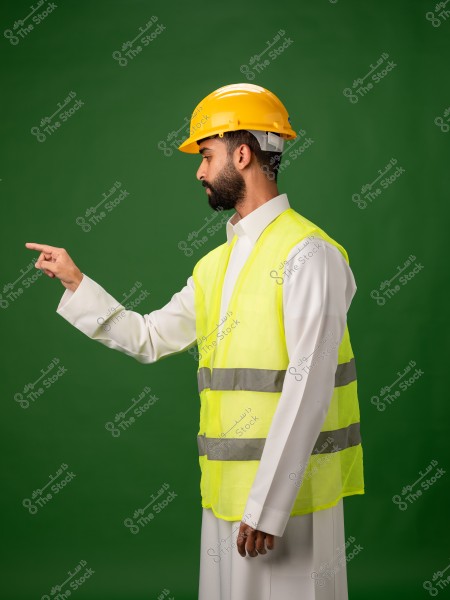 رجل يرتدي خوذة أمان صفراء وسترة عاكسة صفراء يقف أمام خلفية خضراء ويشير بأصبعه.