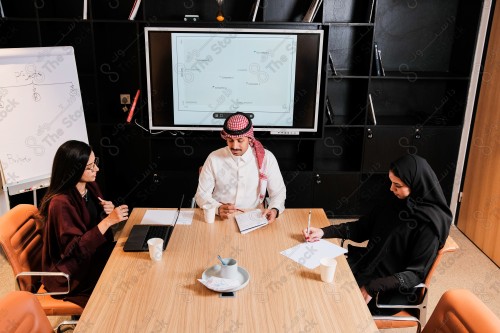 A Saudi man in traditional Saudi dress holds a meeting with Saudi female employees wearing abaya in the meeting room