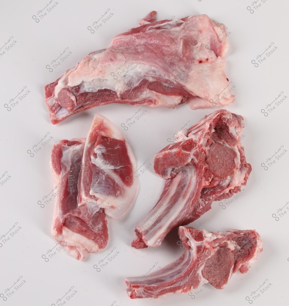 Various cuts of raw lamb placed on a white surface. The image features different types of lamb slices, some with bones and others without, showing a clear contrast between the red meat and white fat.