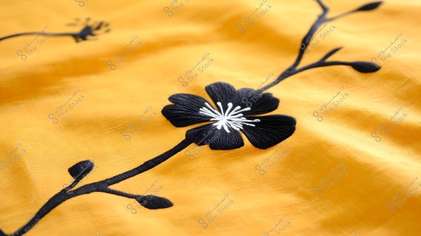 An image of a beautiful flower embroidered with black and white thread on soft yellow fabric. The elegant design features a branch with clean, simple lines, showcasing fine details in the thread color gradients.
