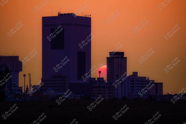 Sunset behind city towers with an orange sky.