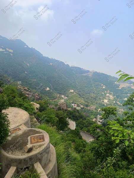 A beautiful landscape of mountains covered in greenery in a mountainous area, with white houses scattered across the slopes. The sky is blue with some clouds, and there are green plants in the foreground.