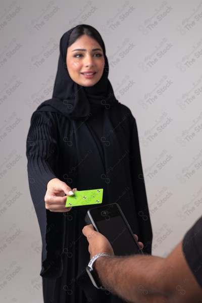 Portrait of a Saudi woman holding a card and making automatic payments on a white background