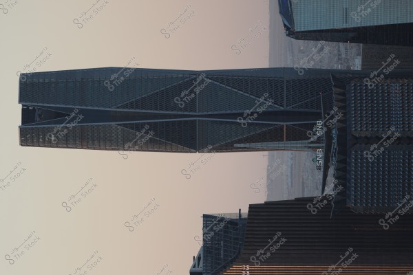 يظهر في الصورة مبنى شاهق مميز بتصميم معماري حديث, يهيمن على المشهد ويلوح في الأفق في مدينة حديثة. المبنى مغطى بواجهة زجاجية ملتفة, ويظهر اسم "SNB" بشكل بارز على واجهته. الأفق في الخلفية يتدرج بلون السماء الغير واضحة المعالم والمباني الأخرى المحيطة بالمبنى.