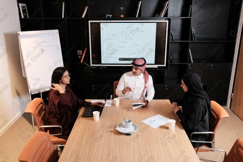 A Saudi man in traditional Saudi dress holds a meeting with Saudi female employees wearing abaya in the meeting room