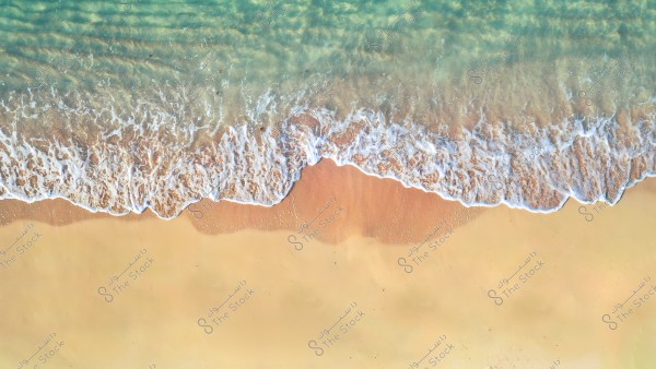 An aerial view of a beach with gentle waves lapping onto the golden sand. The vibrant blue water transitions to white with the foam of the waves.