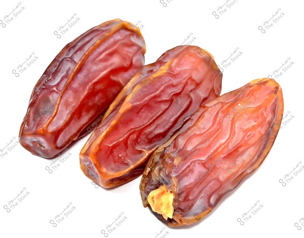 Three dried dates with a dark brown color placed on a white surface.