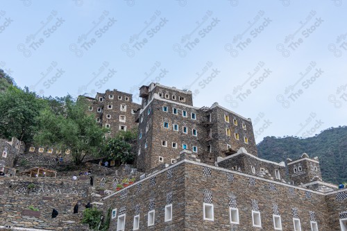 An ancient building built of stones in the middle of a group of windows surrounded by white paint while the sky looks cloudy during sunset, Rijal Almaa Heritage Village in the Asir region