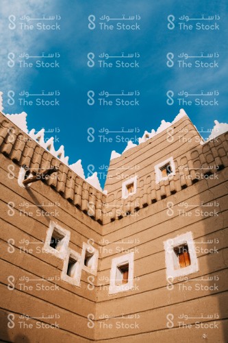 مبنى تراثي مبني من الطين به العديد من النوافذ الخشبية المحاطة بطلاء أبيض في مدينة نجران وتظهر السماء شبه صافية نهارًا
