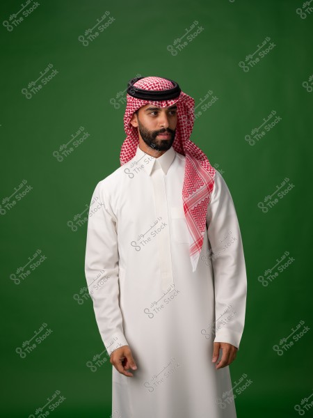 صورة لرجل يرتدي الزي السعودي التقليدي, يتكون من ثوب أبيض وغترة حمراء وبيضاء مع عقال أسود. يقف أمام خلفية خضراء.