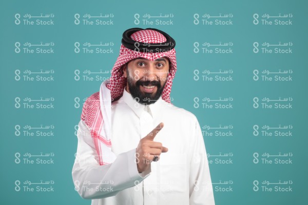 بورتريه رجل سعودي يرتدي الزي السعودي التقليدي ويشير بيده مبتسمًا