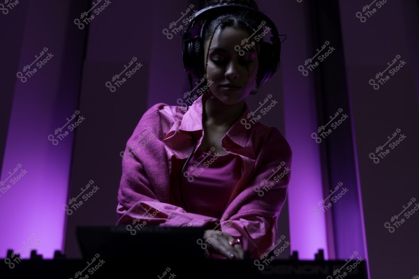 امرأة ترتدي سماعات رأس أمام جهاز دي جي, الأضواء المحيطة خافتة بألوان أرجوانية.