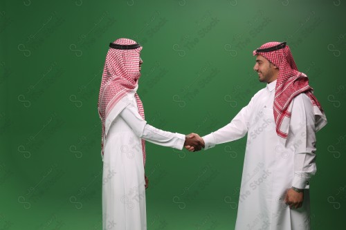 Portrait of two Saudi men in traditional uniform on a green background shaking hands smiling, sad, angry, memorial photos, documenting a happy moment.