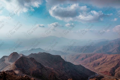 An aerial shot of a series of towering rocky mountains and off-road extended of the mountain. The sky appears overcast during the day. nature in Saudi Arabia