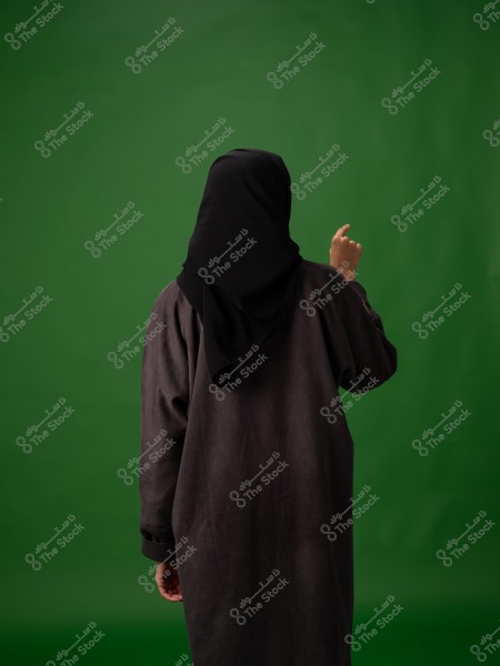 امرأة ترتدي حجابًا أسود تقف أمام خلفية خضراء.