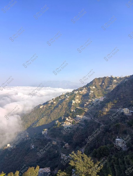A natural landscape showing a series of houses scattered across green mountain slopes, with a layer of white clouds in the horizon. The sky is clear blue at the top, adding a serene and bright atmosphere to the scene.