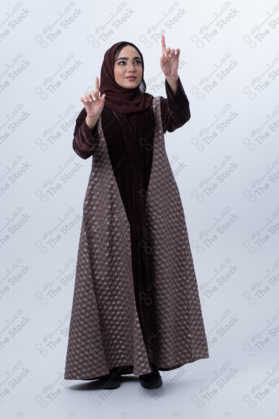 A young Saudi woman wearing an abaya and pointing with her finger. Standing on white background.