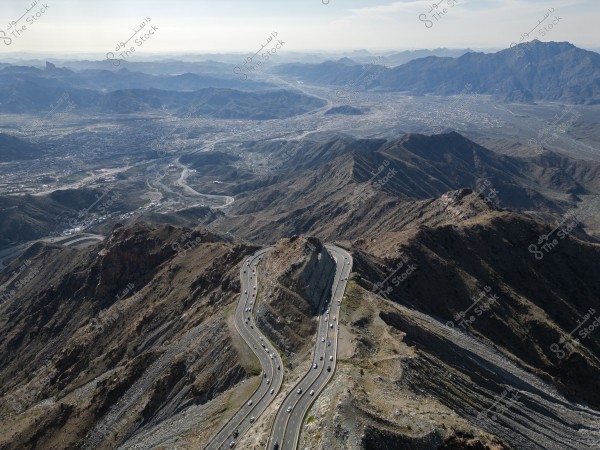 Aerial view of a winding road passing through a range of green mountains in the daytime, stretching into the distant horizon.