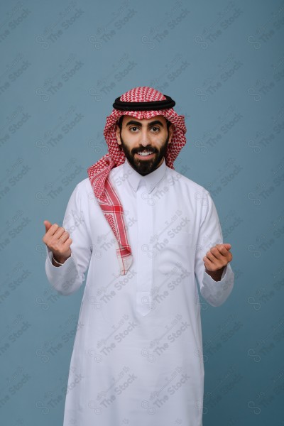 بورتريه شاب سعودي يرتدي الزي السعودي يقوم بالتفاعل بيدية ، ويظهر بتعابير وجه، على خلفية سماويه