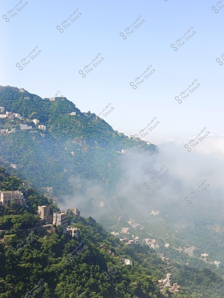 An image of a mountain covered with lush green vegetation in an area with distinctive architectural style. Several traditional buildings are scattered across the slopes, surrounded by clouds adding an air of mystery to the scene. The sky is clear and blue at the top of the image.