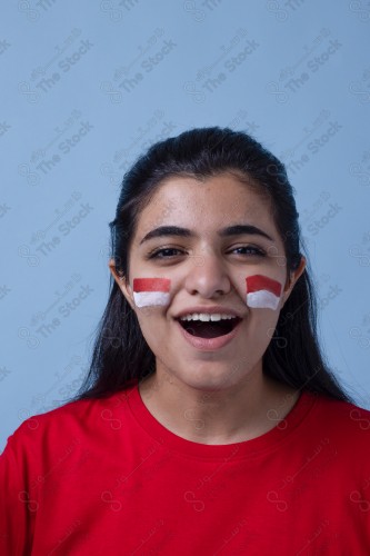 Portrait of a Saudi woman wearing a red T-shirt cheering the football team on a blue background and showing expressions of joy and enthusiasm, World Cup.