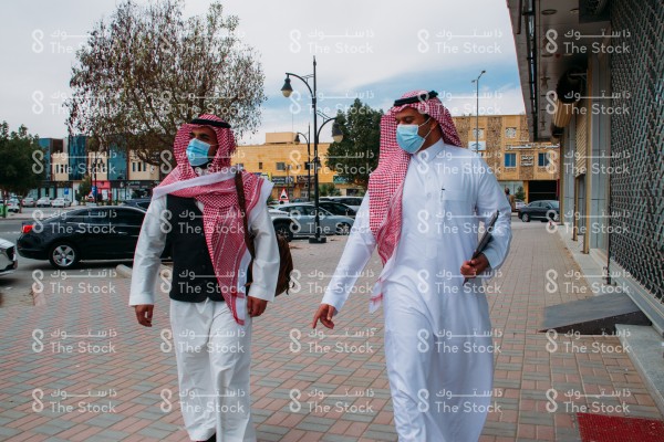 رجال بالزي السعودي يرتدون الكمامة يتحدثون وهم بالرصيف