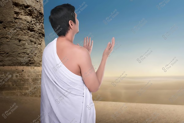 شخص يرتدي إحراماً أبيض اللون يقف ويبدو وكأنه يصلي أو يدعو, مع خلفية تظهر جزءًا من بناء أثري وصحراء شاسعة تحت سماء زرقاء.

-
