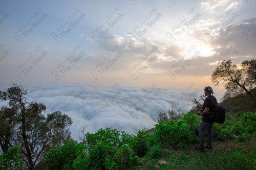 رجل سعودي واقف بجبل الأسود ممسك بالكاميرا يلتقط صورة الطبيعة في جازان