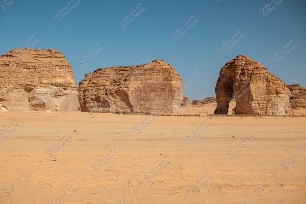 Image showing massive rock formations in a yellow sandy desert under a clear blue sky. The rocks have varying shapes and sizes, appearing carved by wind and weather over time.