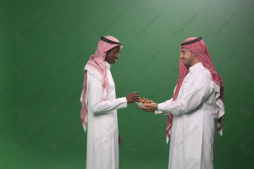 رجل سعودي يرتدي الثوب و الشماغ يقوم بتقديم الحلوى لرجل سعودي اخر