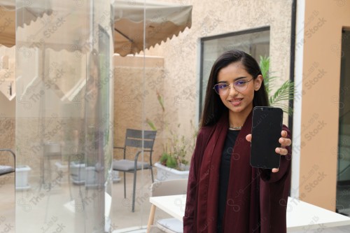 A Saudi woman wearing an abaya holds a mobile phone and displays its screen