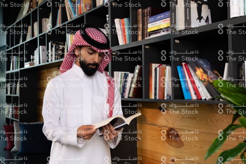 رجل سعودي يرتدي الزي السعودي التقليدي يتصفح أحد الكتب في المكتبة