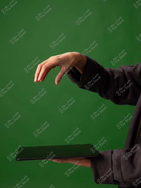 يد أنثى تمسك بجهاز لوحي أمام خلفية خضراء.