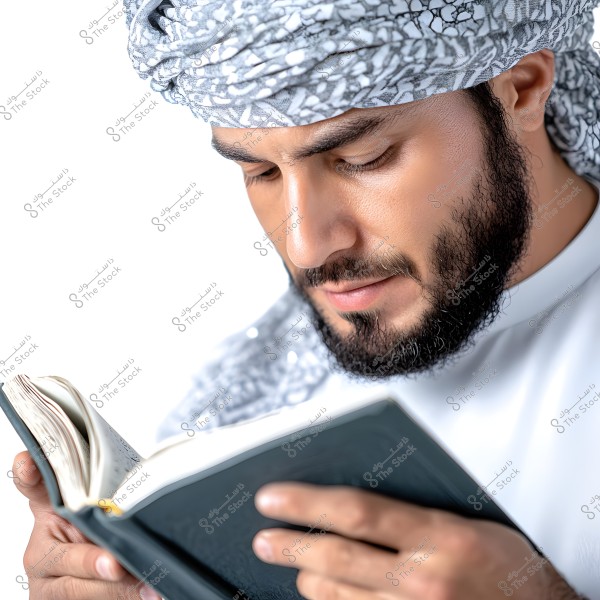 A portrait of a man in traditional attire reading a book. He is wearing a patterned ghutra and agal, along with a white shirt. His focus is on the open book in his hands, and his face shows concentration.