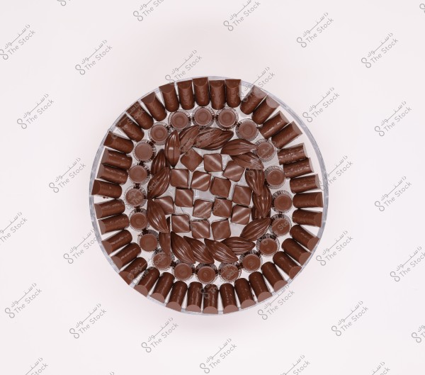 Image of a circle made of intricately arranged chocolates within a glass dish, featuring conical, square, and oval shapes, distributed in an artistic and symmetrical design.