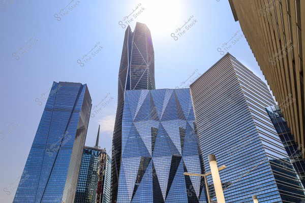 An image of a cluster of reflective glass skyscrapers on a sunny day with a clear blue sky. The architectural design of the buildings is intricate, featuring triangular details and smooth surfaces. The bright sunlight in the background enhances the visual impact of the buildings.