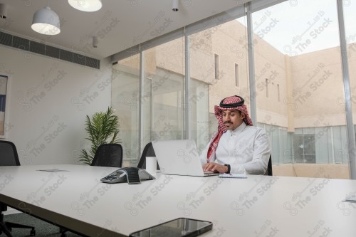 A Saudi man wearing the Saudi thobe sits in the meeting room and uses the mobile device