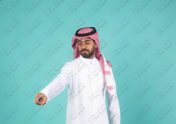 شاب سعودي على خلفية تركوازيه يعمل اشارات بيده، يشير باتجاه اليمين، ثوب و شماغ