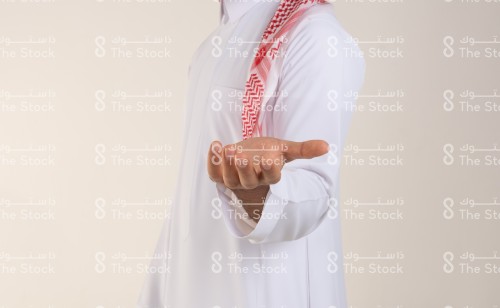 يد شاب سعودي يرتدي الزي السعودي التقليدي يمد ذراعه ويفتح كفه للأمام