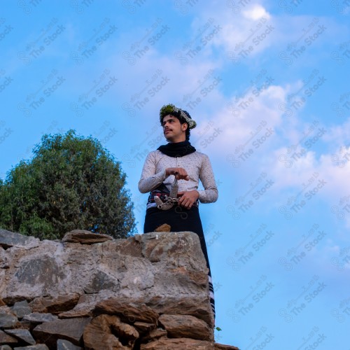 A Saudi man wearing a traditional dress at the top of the mountain and behind him clouds appear in Jizan