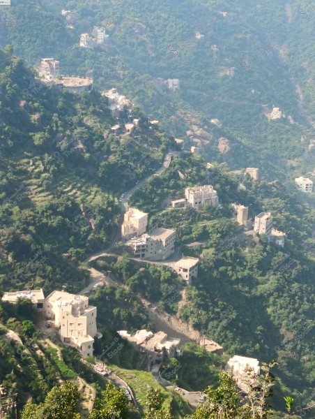 A natural landscape of green mountains with hills, dotted with small white houses amidst nature. The greenery is dense and some of the houses are in traditional building styles.