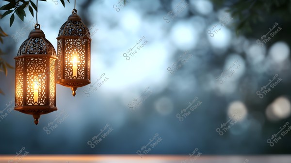 Two ornate metal lanterns hanging from a tree, illuminated with a warm glow. The background features a soft bokeh effect with blue and green hues, highlighting the intricate details of the lanterns.