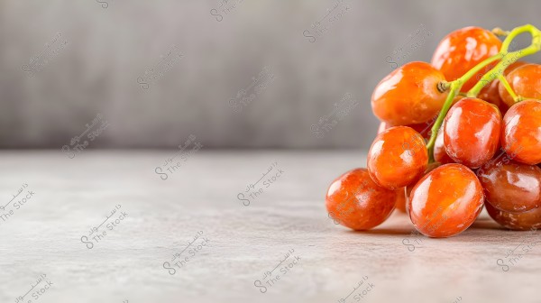 A cluster of glossy red grapes placed on a light-colored marble surface, with a blurred gray background. The grapes appear ripe and plump.