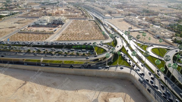 تصوير جوي لحركة سير السيارات على الطريق السريع في مدينة الرياض، الفن الهندسي المعماري للمجسمات الفنية على شكل أشجار خضراء، الطرق المتقاطعة في دوار عرقة بالمملكة العربية السعودية، البنية التحتية المتطورة